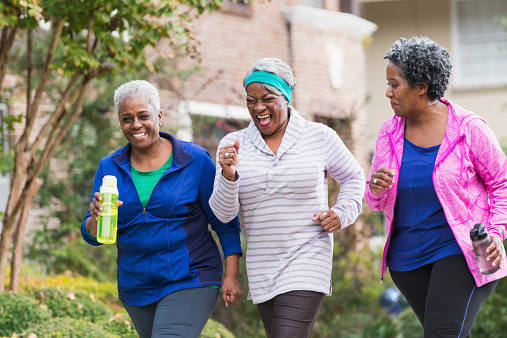 A group of three senior African America women exercising together, jogging or power walking along a sidewalk in a residential neighborhood.  They are having fun, laughing.
